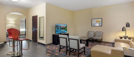 A hotel room with a TV, seating area, and a patterned carpet.