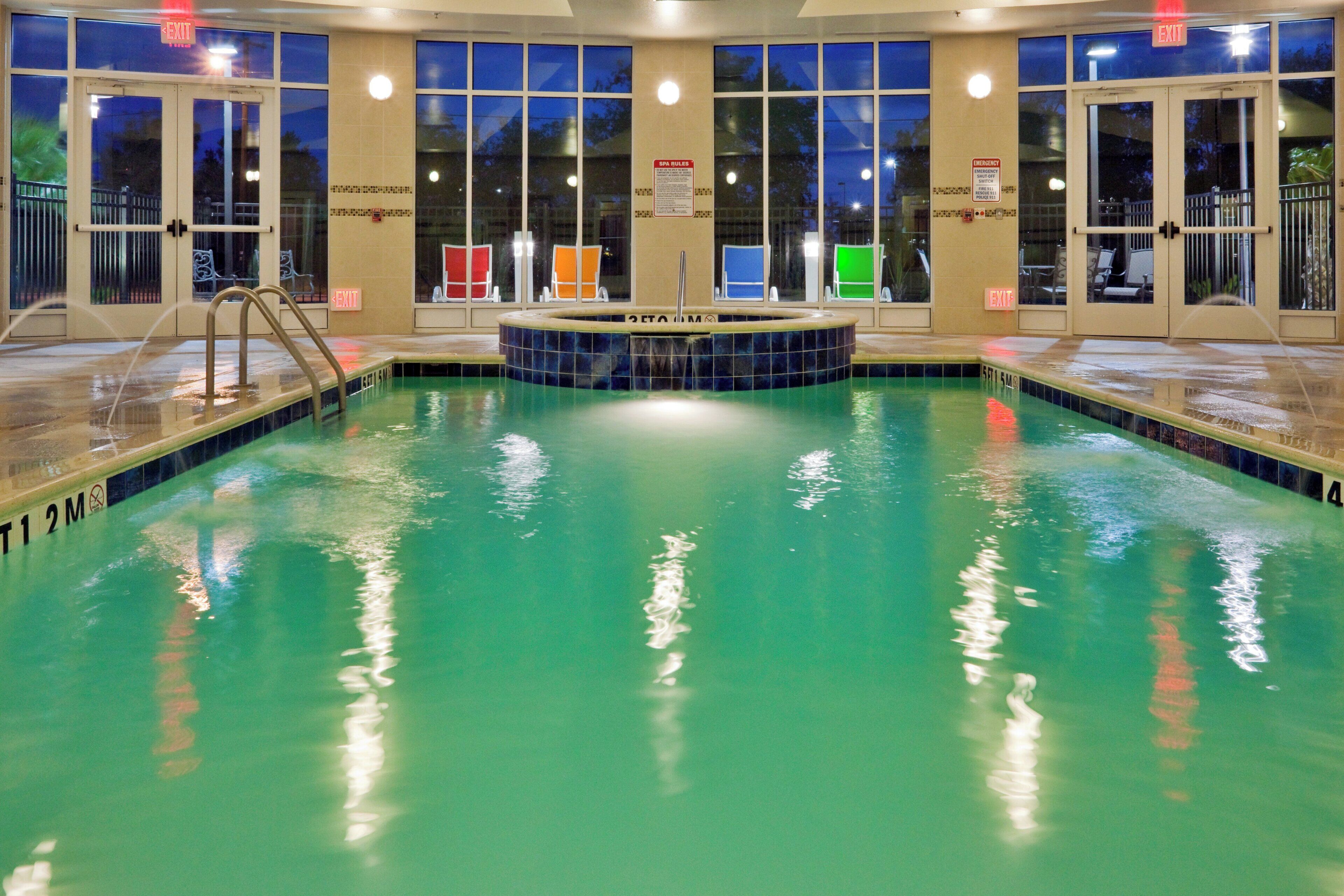 A swimming pool with multiple exits, a hot tub, and a view of the outside at night.