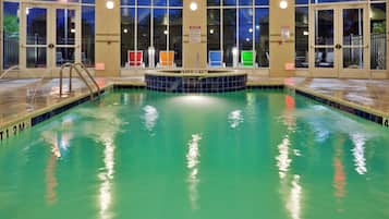 A swimming pool with multiple exits, a hot tub, and a view of the outside at night.