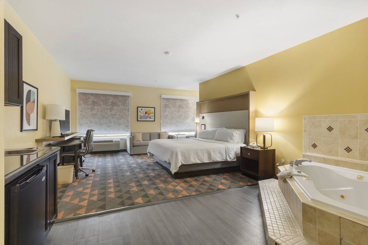 A hotel room with a bed, desk, chair, and a large bathtub.