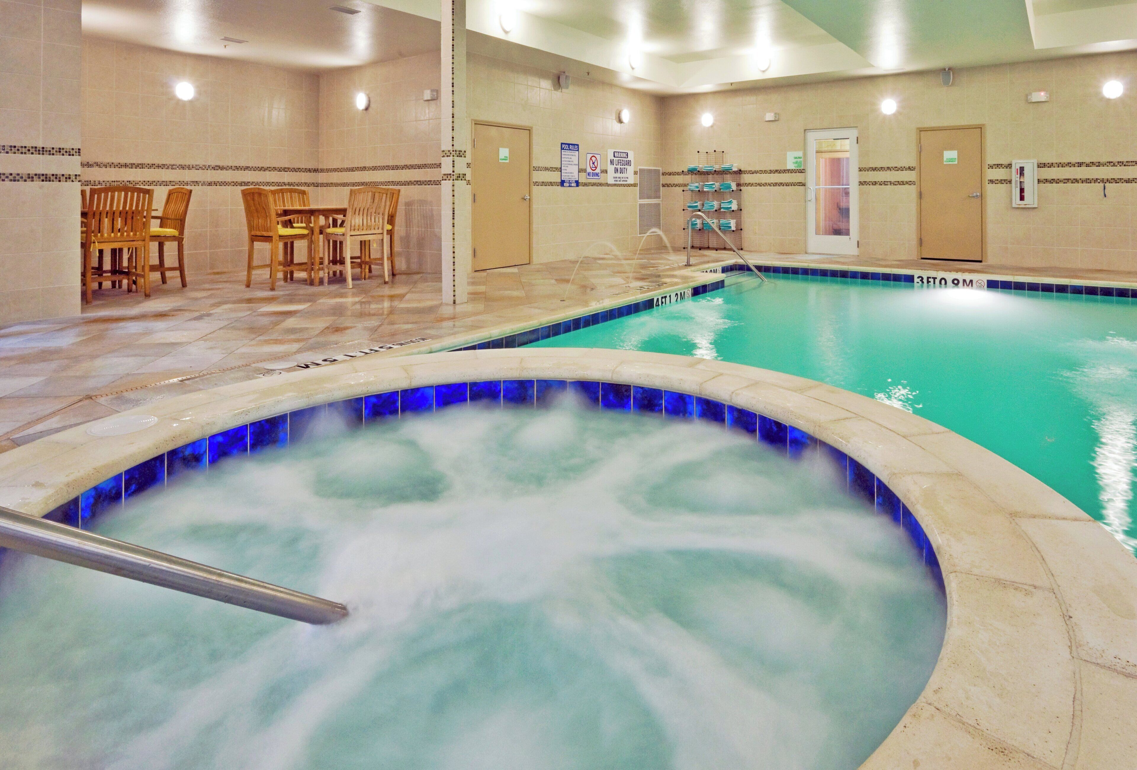 A swimming pool with a hot tub area, tiled walls, and a seating area with chairs.