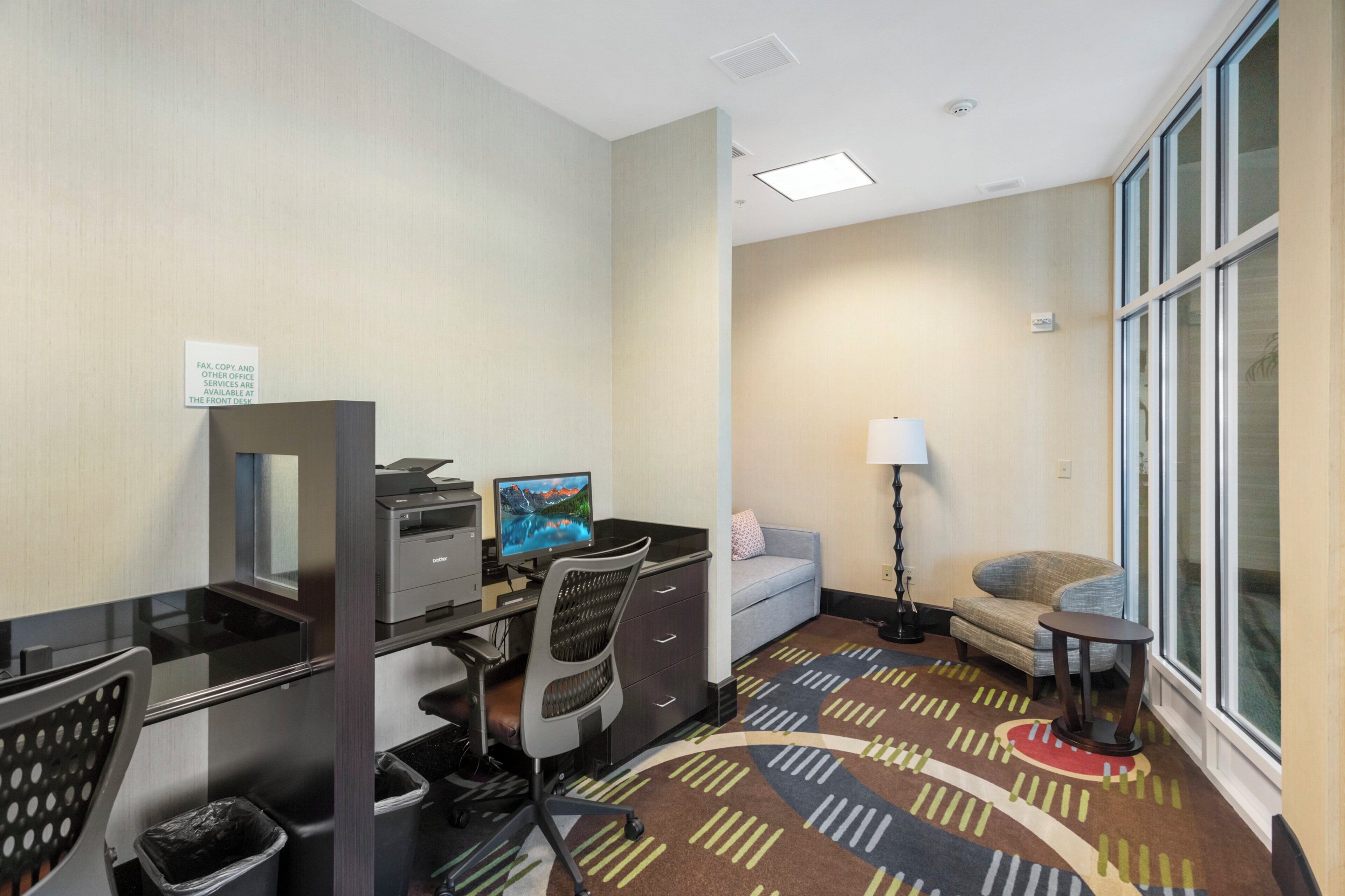 A hotel room with a desk, computer, chair, and a sofa.