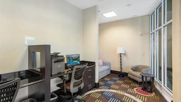 A hotel room with a desk, computer, chair, and a sofa.