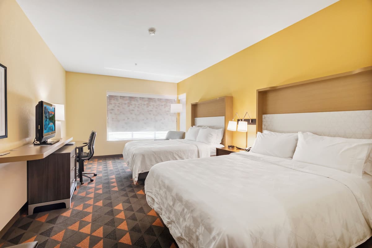 A hotel room with two beds, a desk with a computer, a chair, and a window with a view.