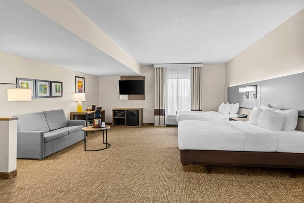 A hotel room with a bed, a sofa, a desk, a TV, and a window with curtains.