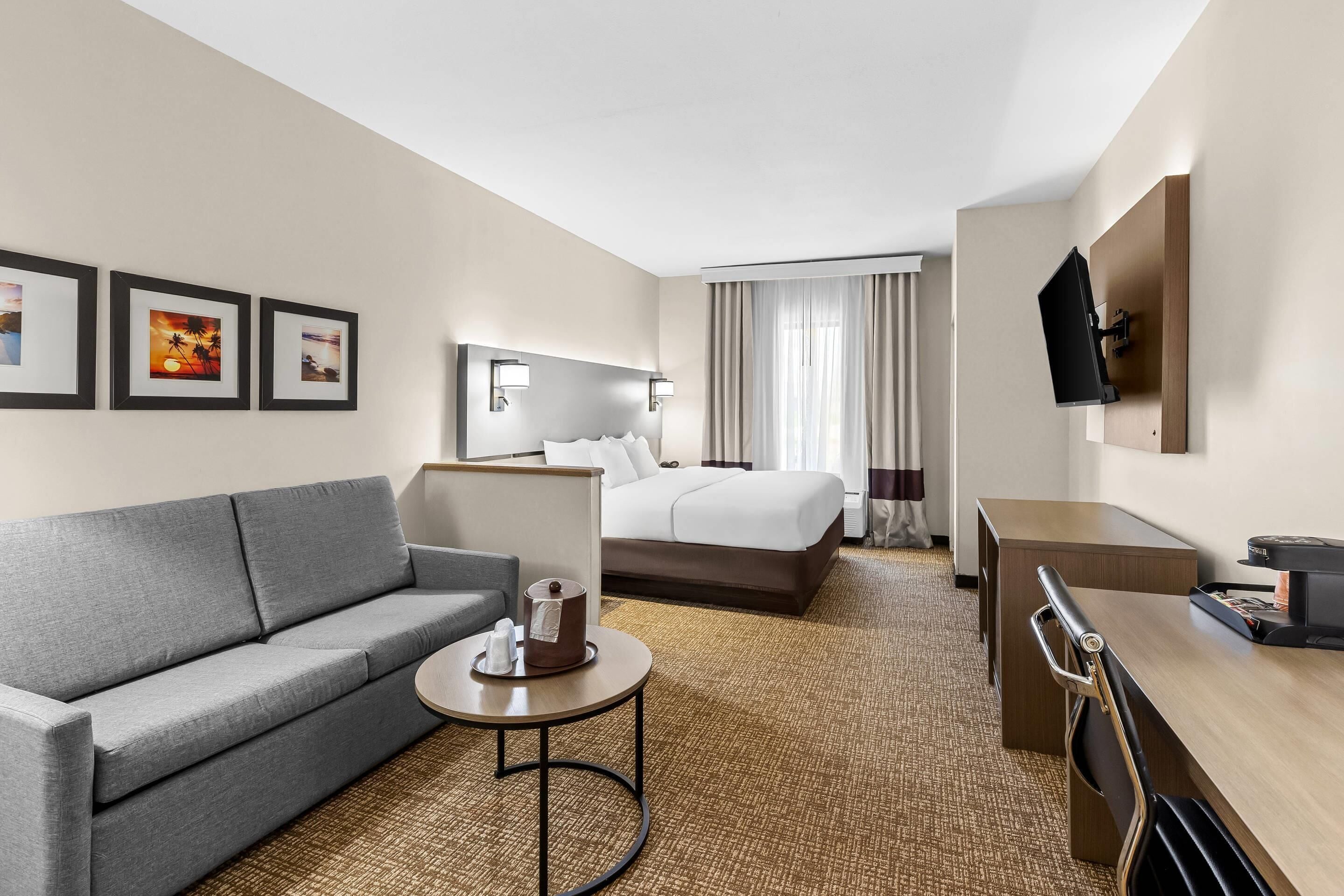 A hotel room with a bed, a sofa, a desk, a TV, and framed pictures on the wall.