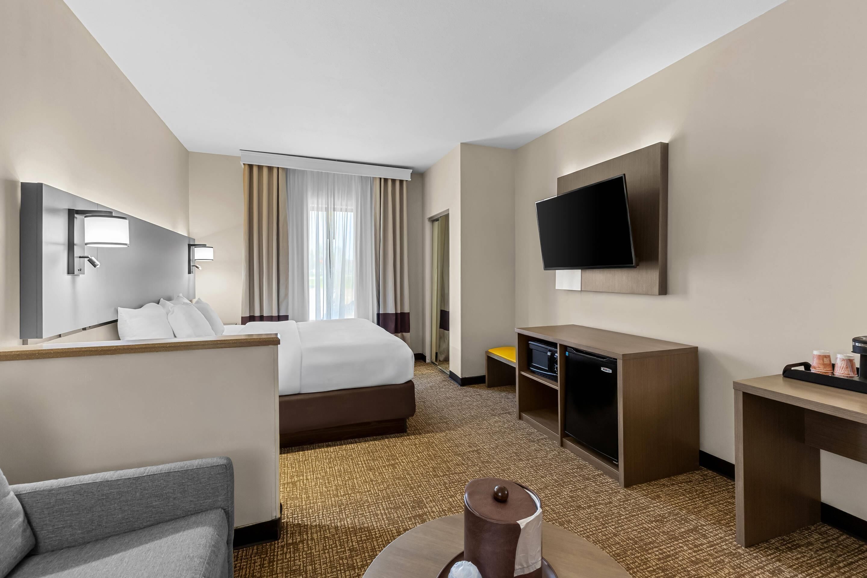 A hotel room with a bed, a desk, a television, a chair, and a small table with a lamp.