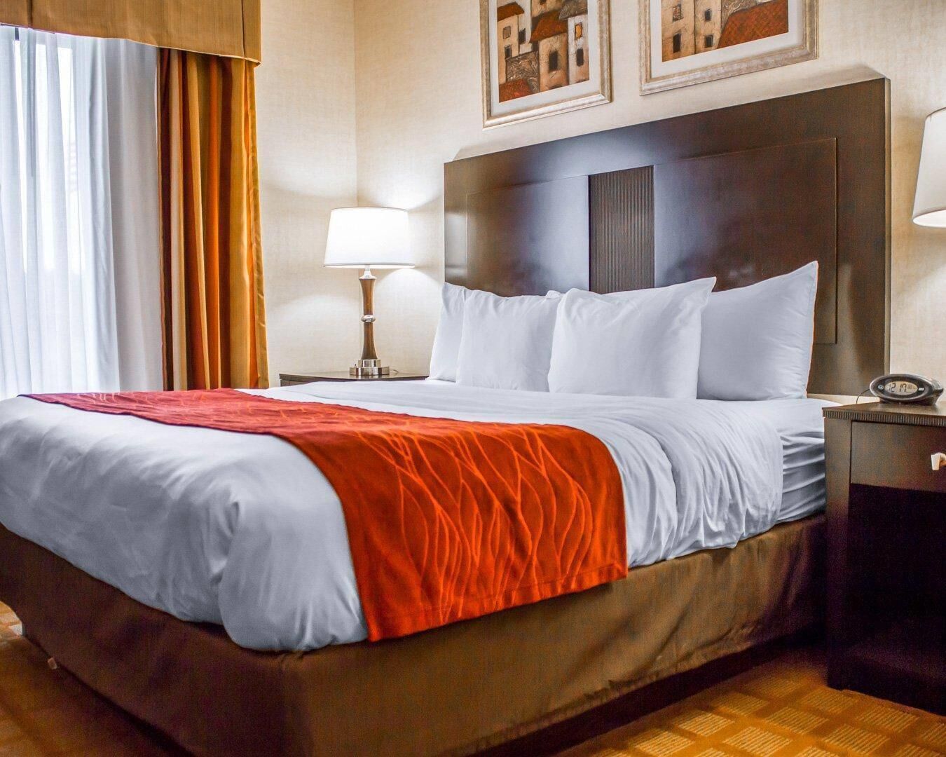 Una habitación de hotel con una cama grande, una mesita de noche con lámpara y un reloj.