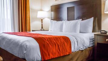 Una habitación de hotel con una cama grande, una mesita de noche con lámpara y un reloj.