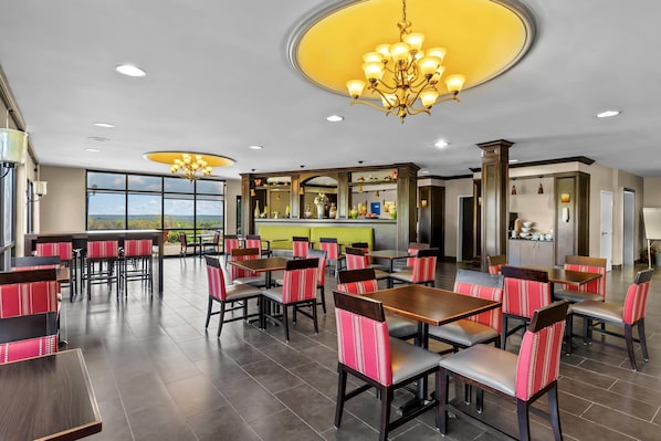Un comedor amplio con varias mesas y sillas, una zona de bar y grandes ventanales con vistas.