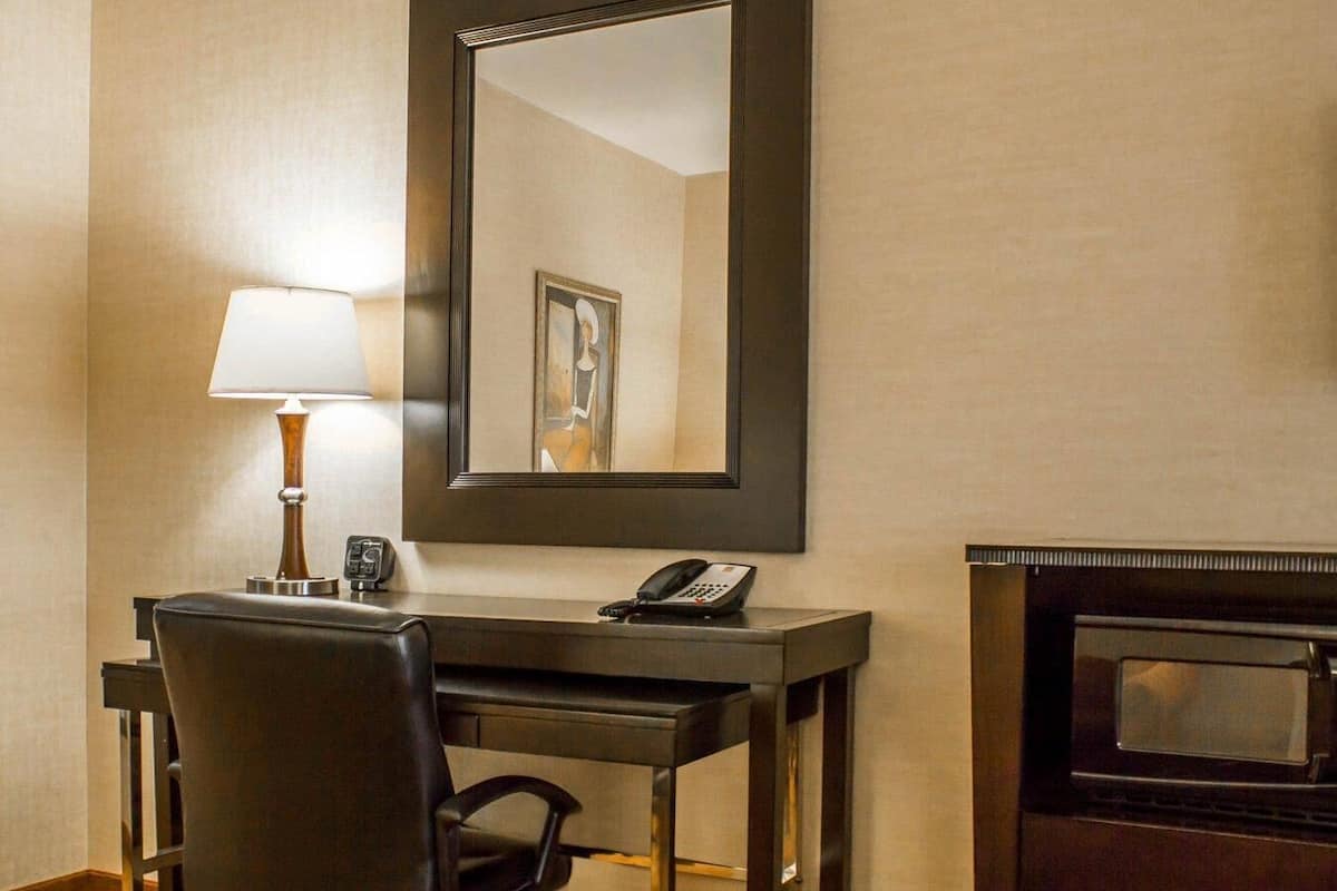 A hotel room with a desk, chair, lamp, telephone, and a mirror.