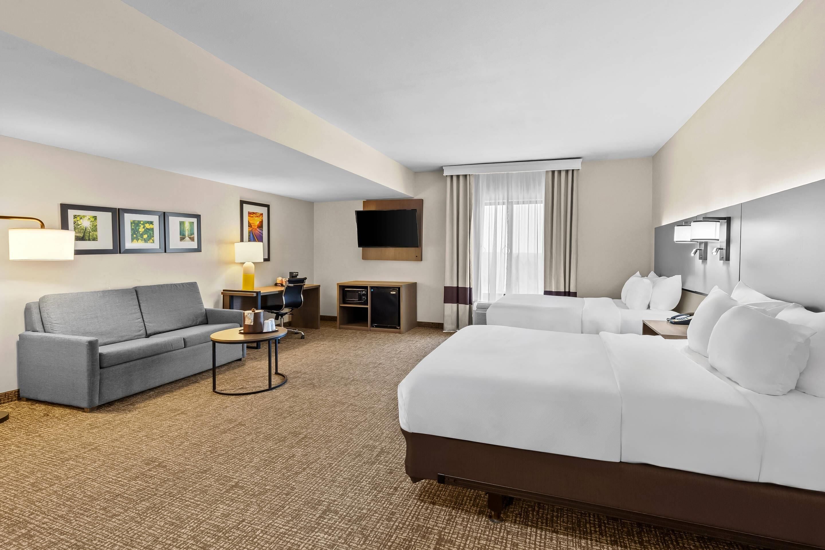 Ein Hotelzimmer mit einem großen Bett, einem Sofa, einem Schreibtisch, einem Fernseher und gerahmten Bildern an der Wand.