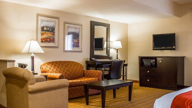 Habitación de hotel con sofá, sillón, escritorio, televisión y cama.