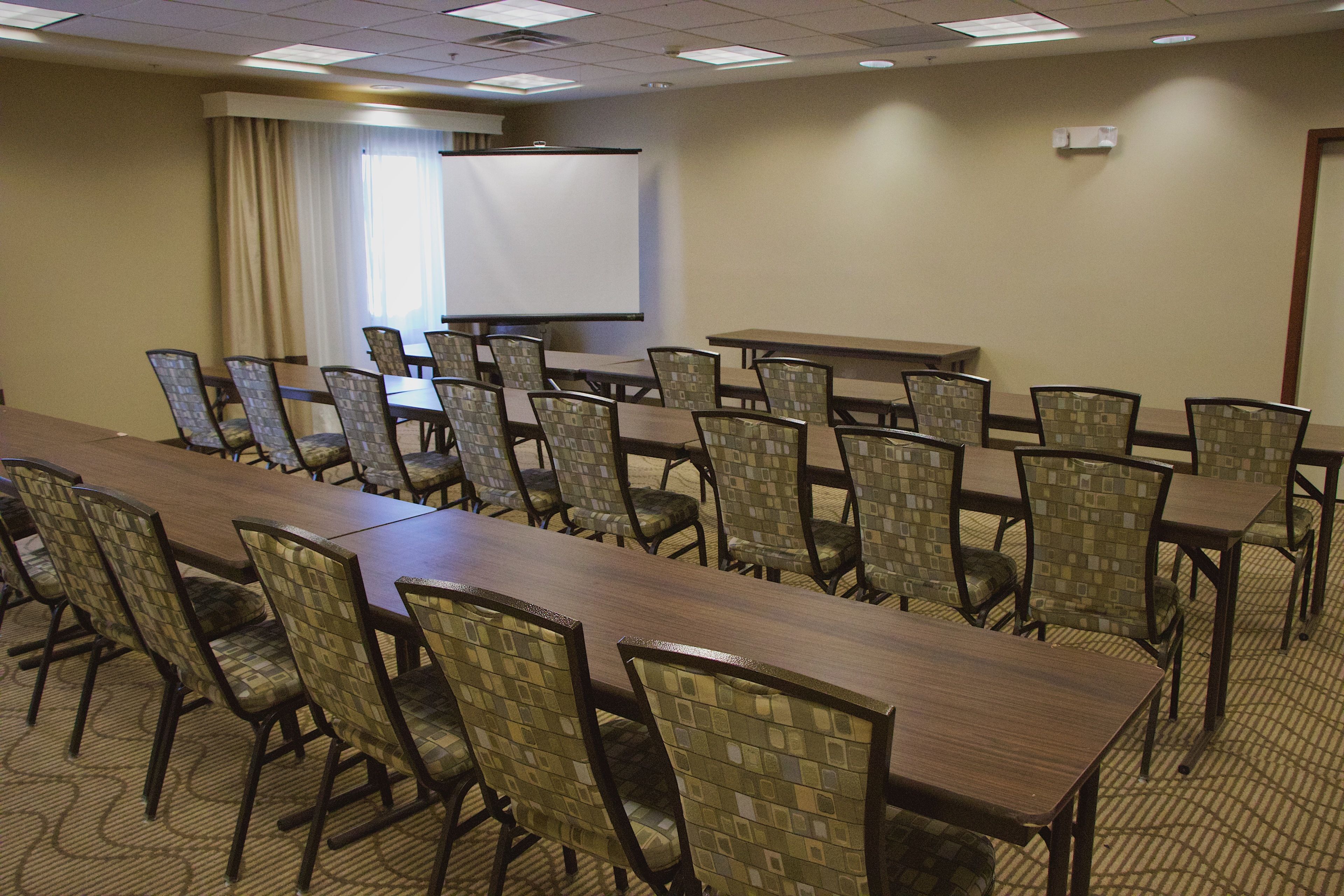 A conference room with a long table and chairs, a projector screen, and a window with curtains.