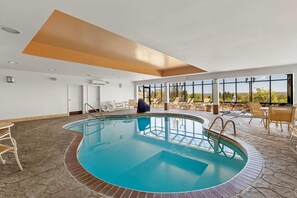 An indoor swimming pool with a stone-tiled floor, a clear blue pool, and a view of the outdoors through large windows. - Comfort Suites Edinboro (Edinboro)
