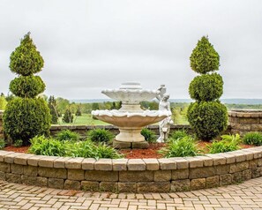 A garden with a central fountain, surrounded by a stone wall and trimmed hedges.
