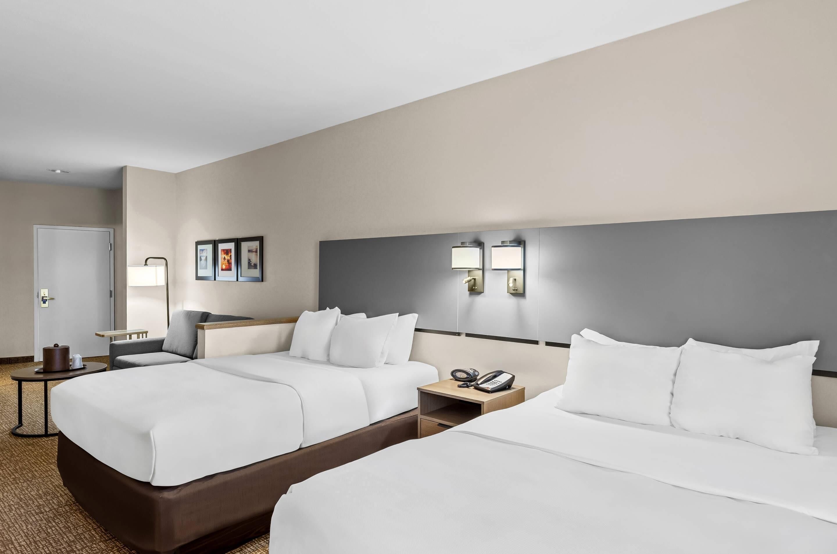 A hotel room with two beds, a bedside table with a phone, a lamp, and a small table with a coffee pot.