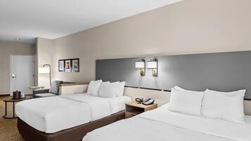 A hotel room with two beds, a bedside table with a phone, a lamp, and a small table with a coffee pot.