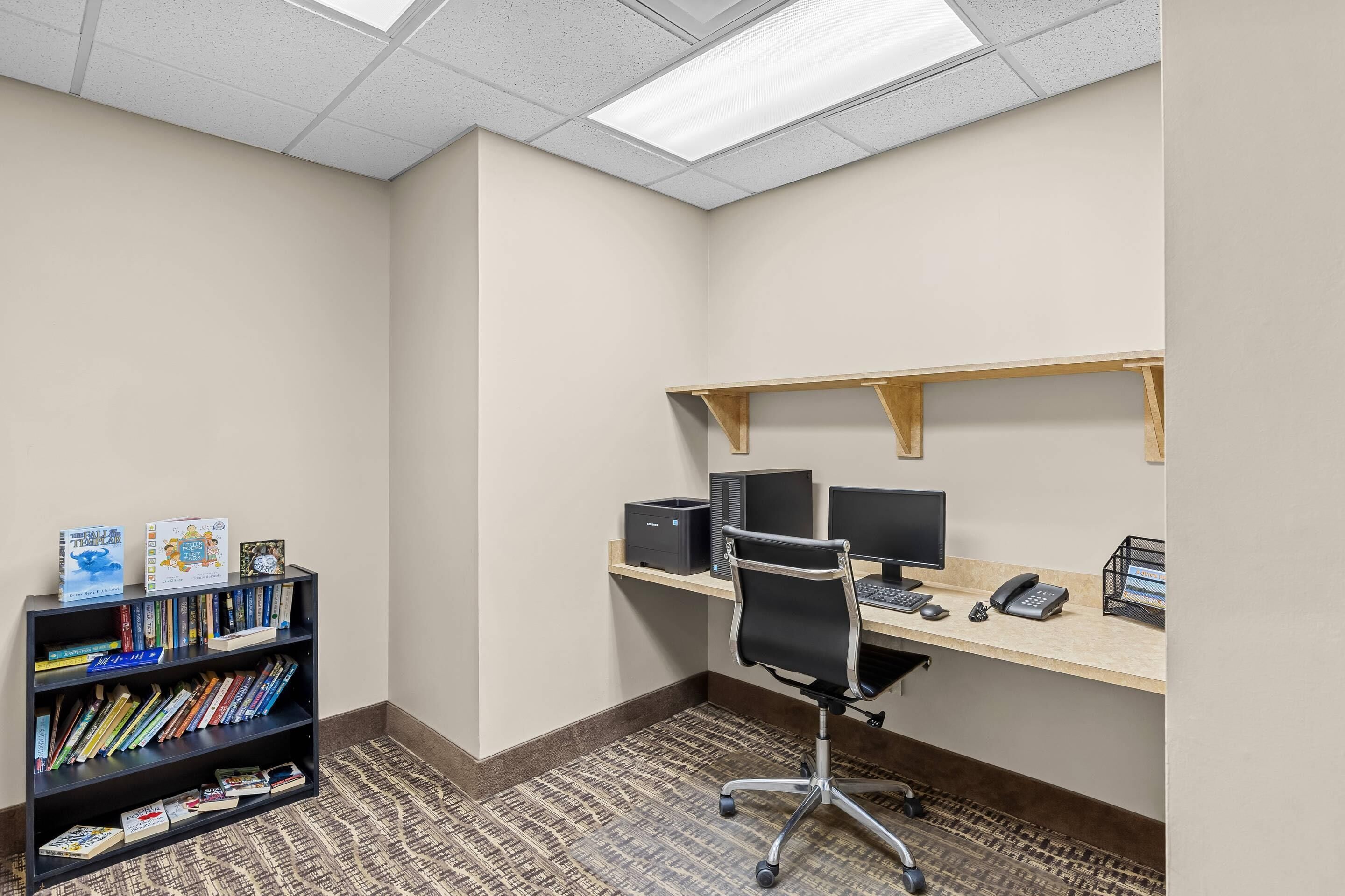 Ein Arbeitsplatz mit Schreibtisch, Computermonitoren, Telefon und Bücherregal.