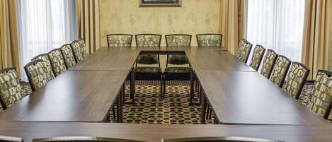 Une salle de conférence avec une longue table et des chaises, des tableaux encadrés accrochés au mur et des rideaux aux fenêtres.