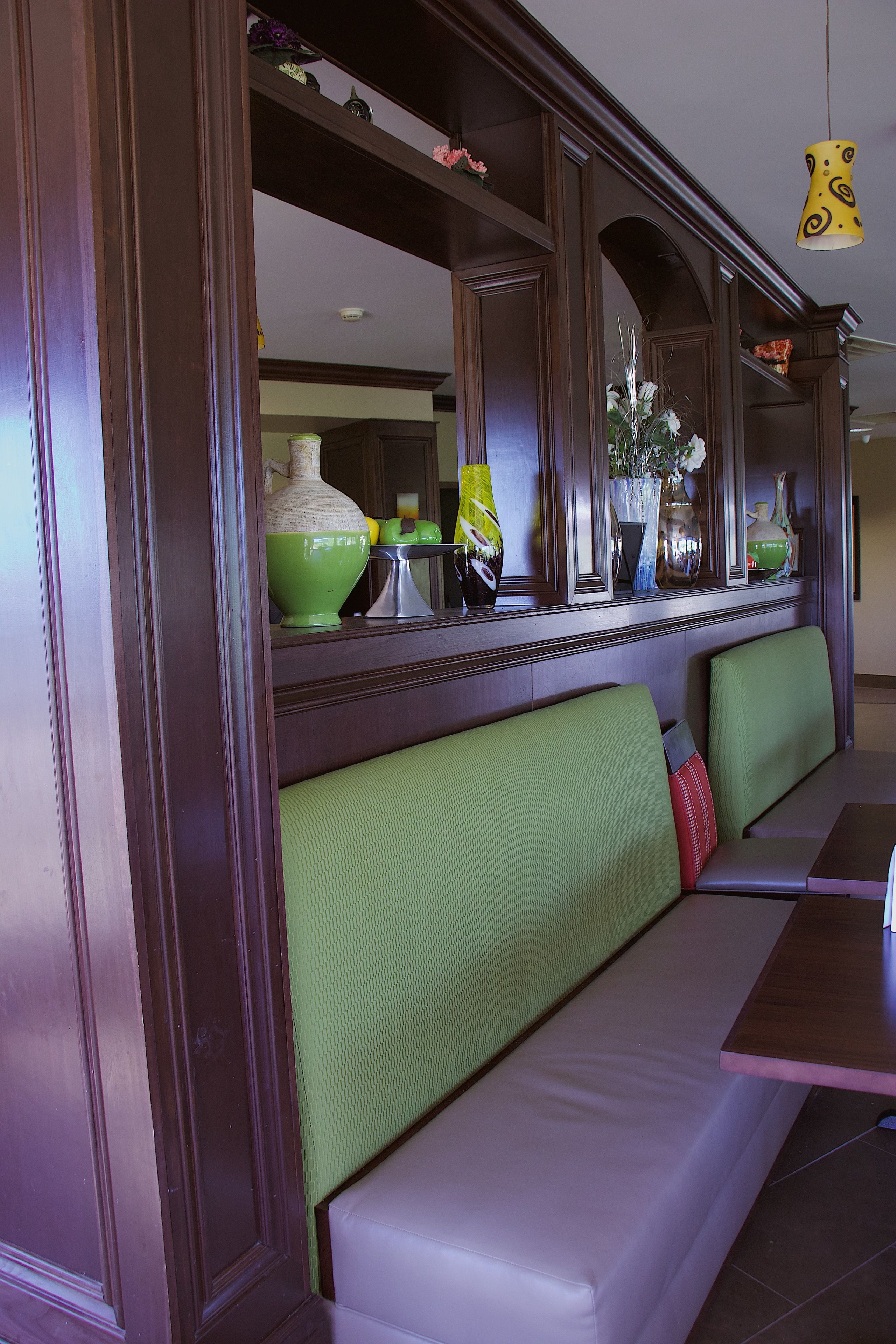 A restaurant with a green booth seating area, wooden paneling, and a yellow hanging light fixture.