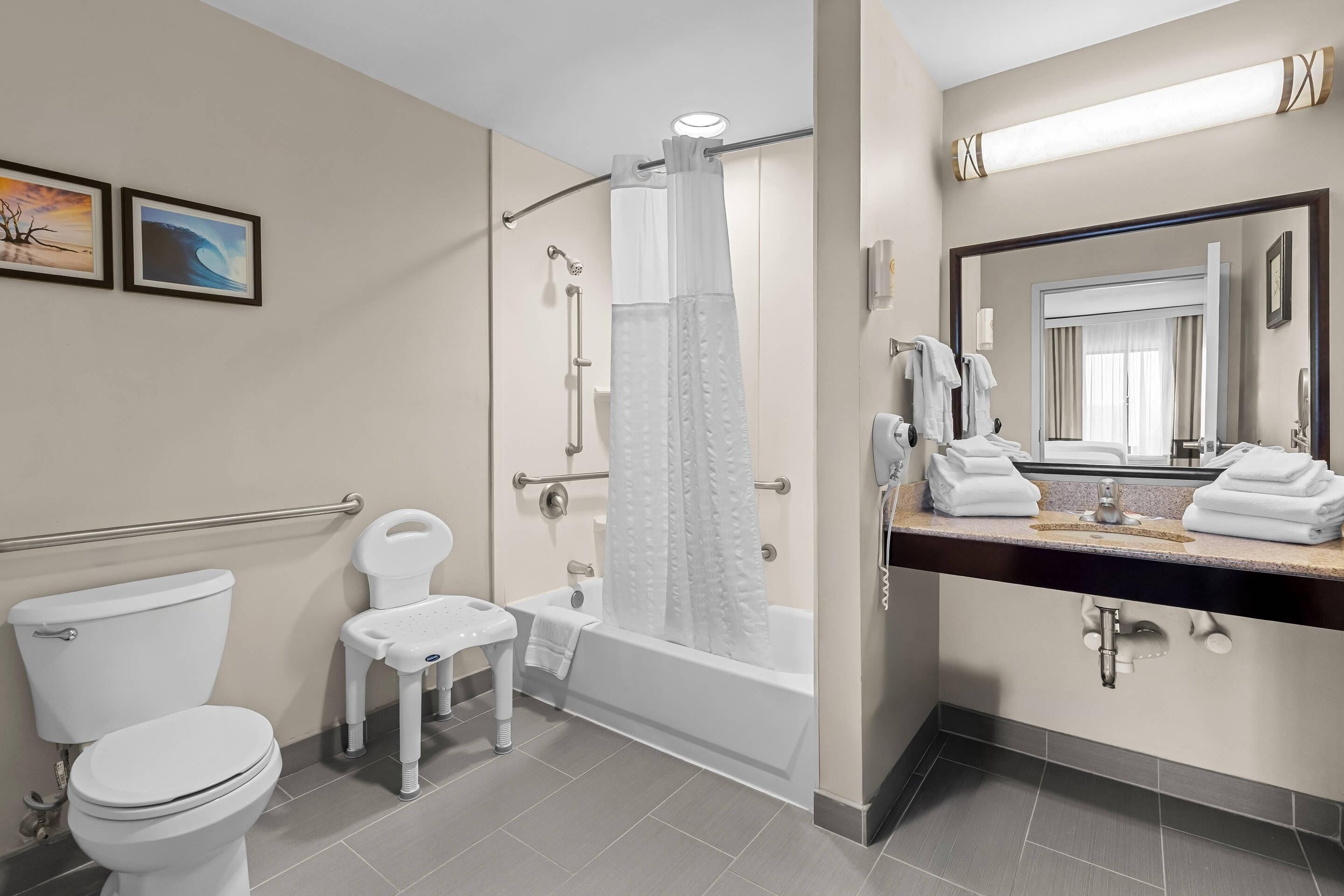 A modern bathroom with a toilet, a shower with a glass door, a vanity with a mirror, and two framed pictures on the wall.