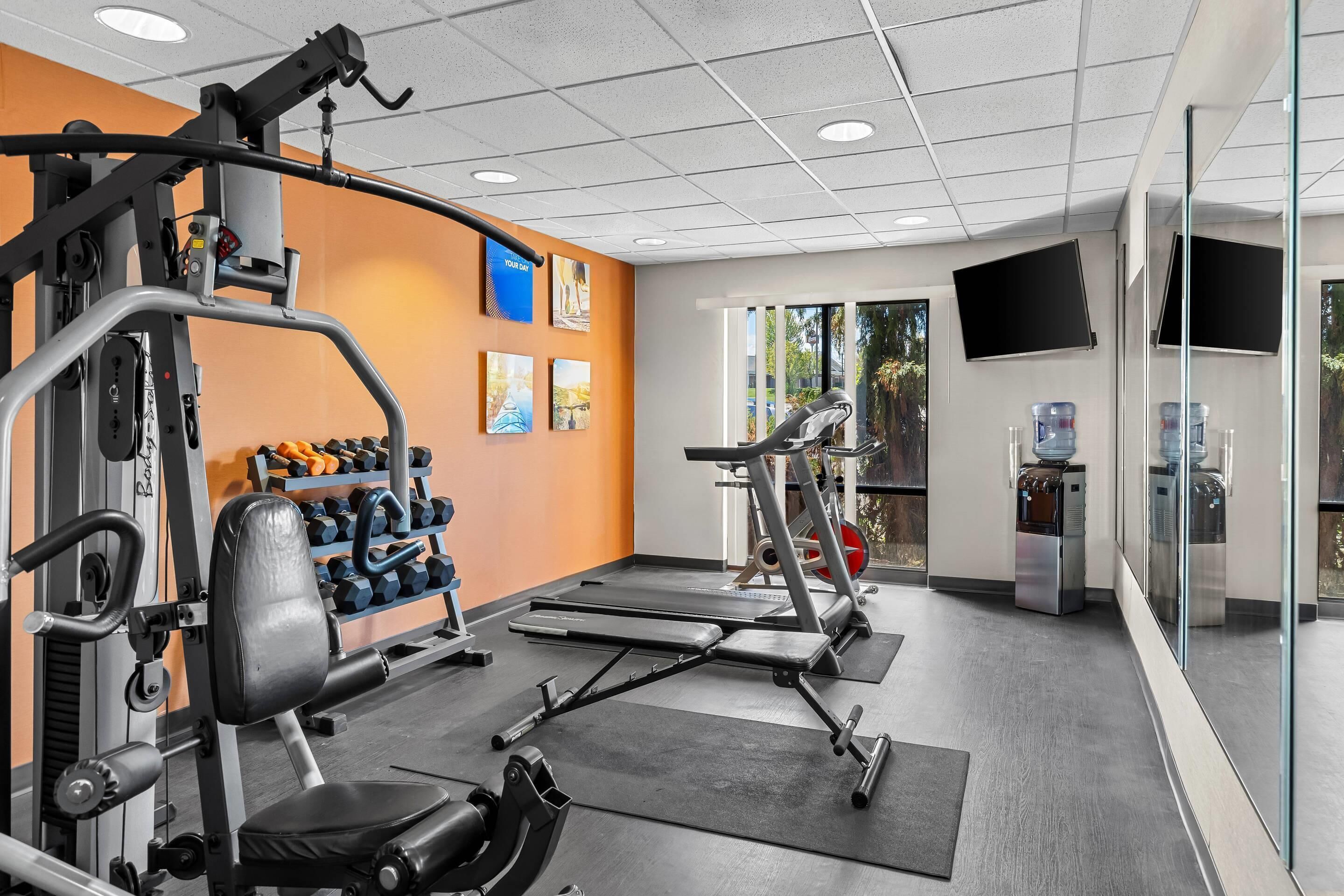 A gym with exercise equipment, a water dispenser, and a TV on the wall.