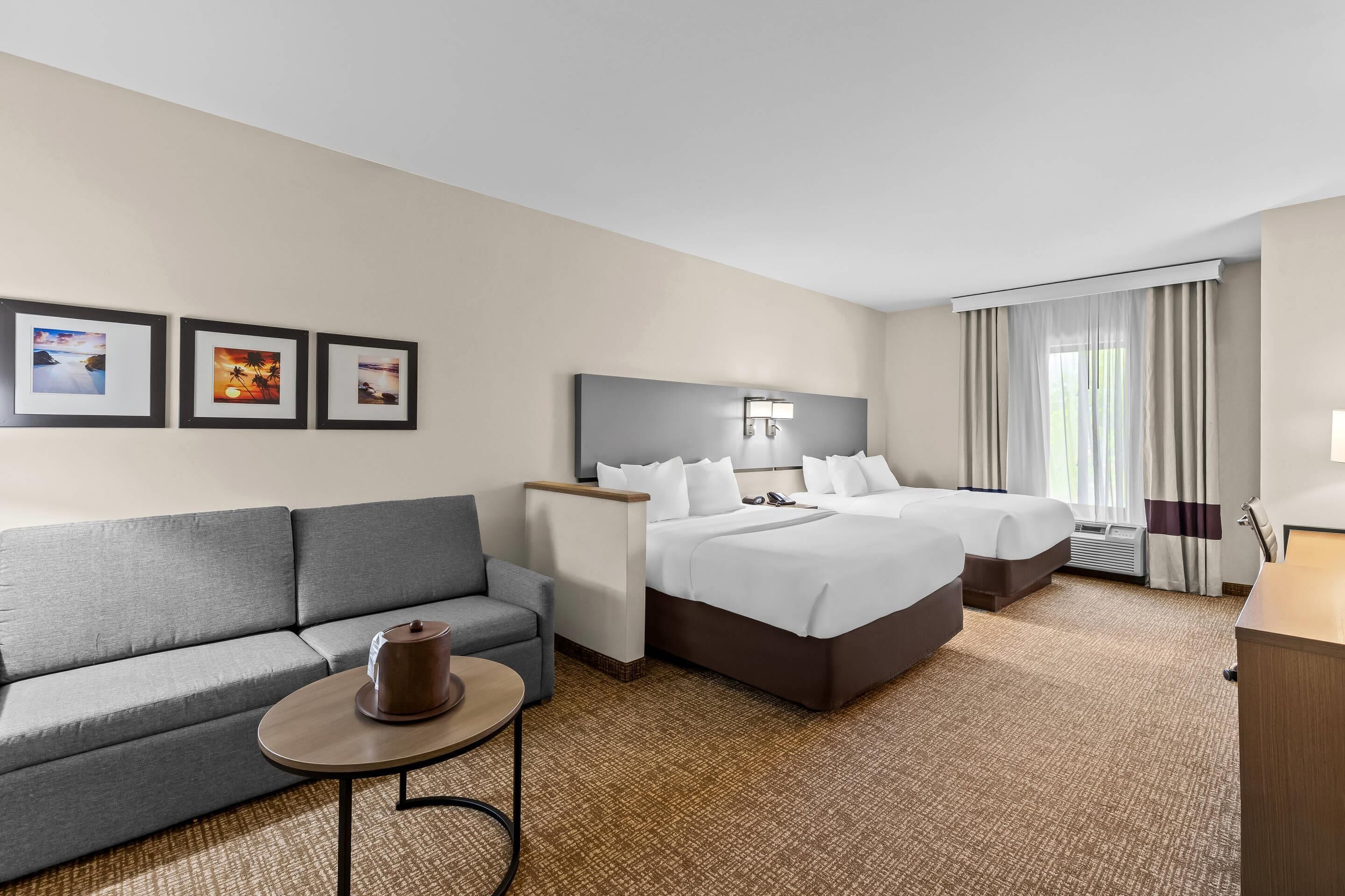 A hotel room with two beds, a sofa, a small table, and framed pictures on the wall.
