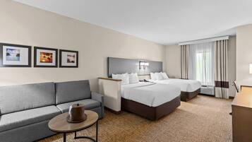 A hotel room with two beds, a sofa, a small table, and framed pictures on the wall.