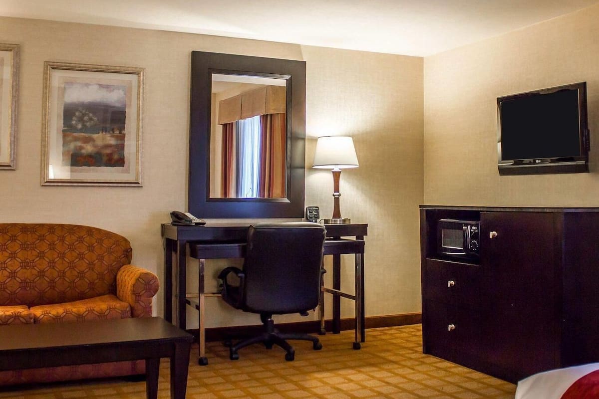 A hotel room with a sofa, a desk with a lamp, a television, and a cabinet.