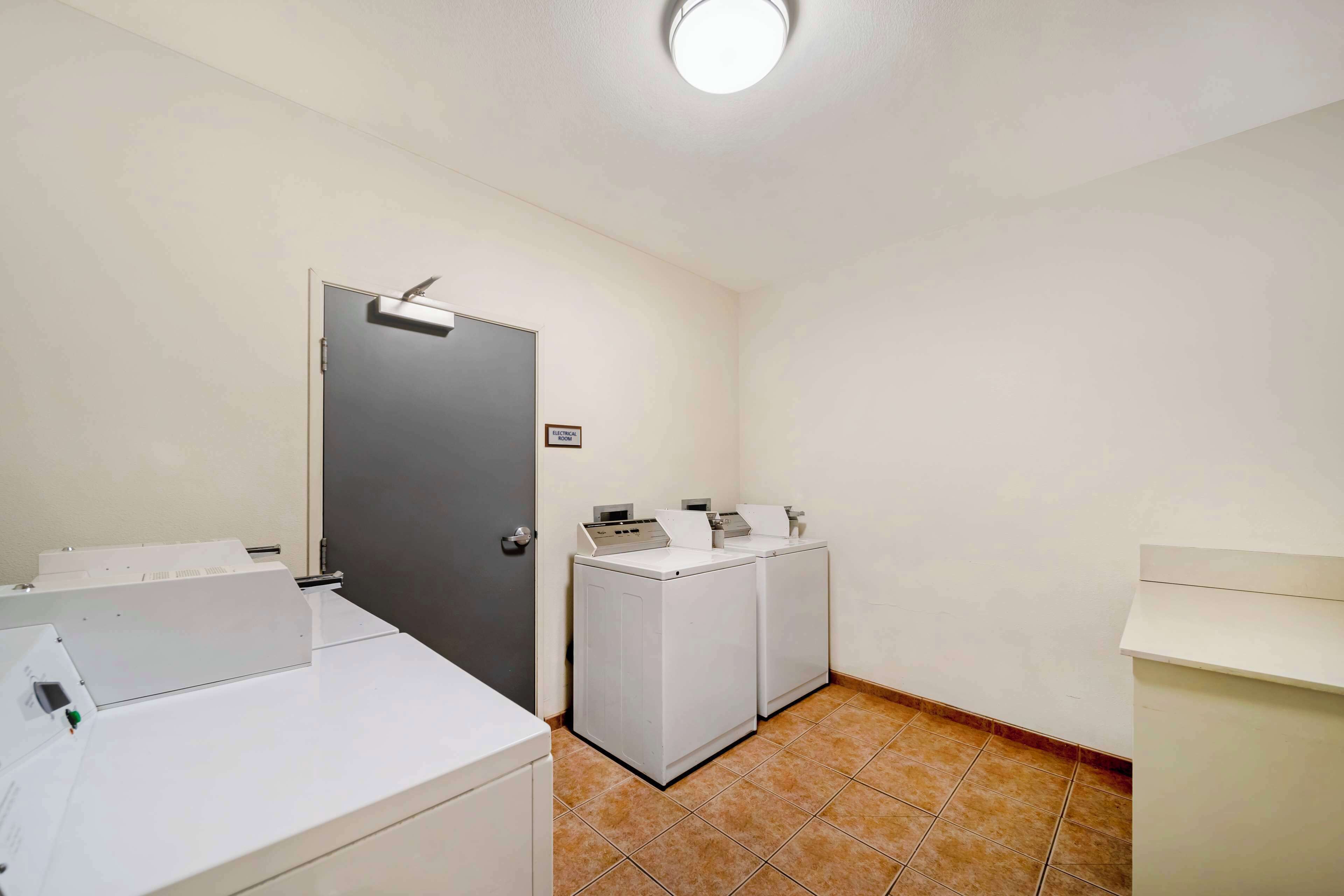 A laundry area with two washing machines and a dryer, a door with a sign, and a tiled floor.