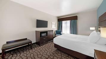 A hotel room with a large bed, a bench, a TV, a desk, and a window with curtains.