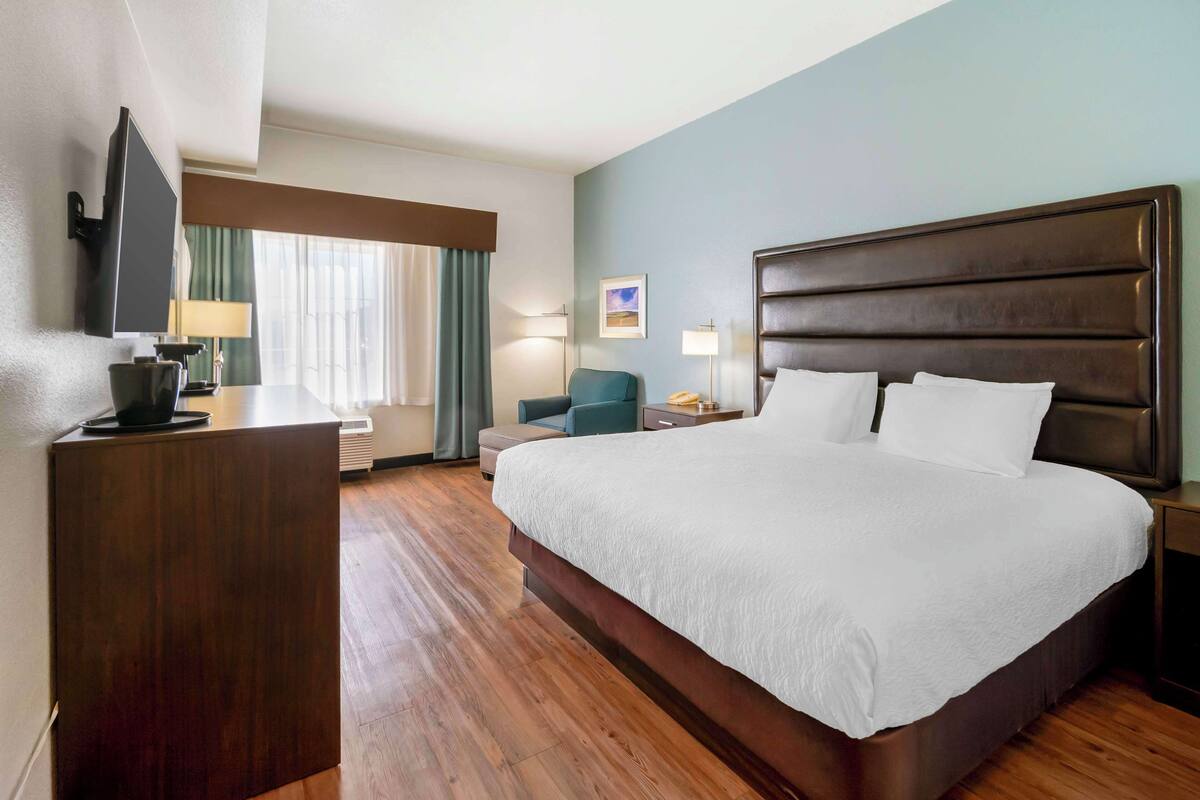 A hotel room with a large bed, a desk, a chair, a TV, and a window with curtains.