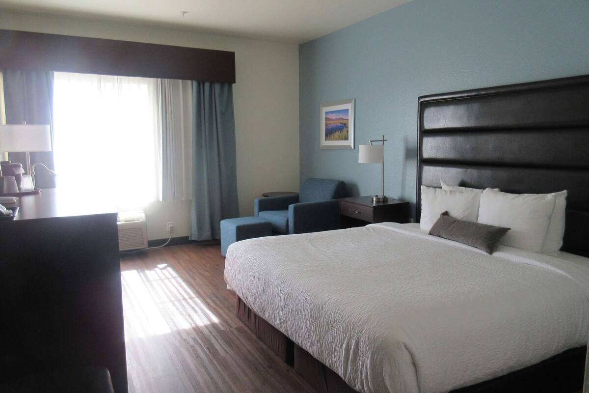 A hotel room with a large bed, a desk, a chair, a lamp, and a painting on the wall.