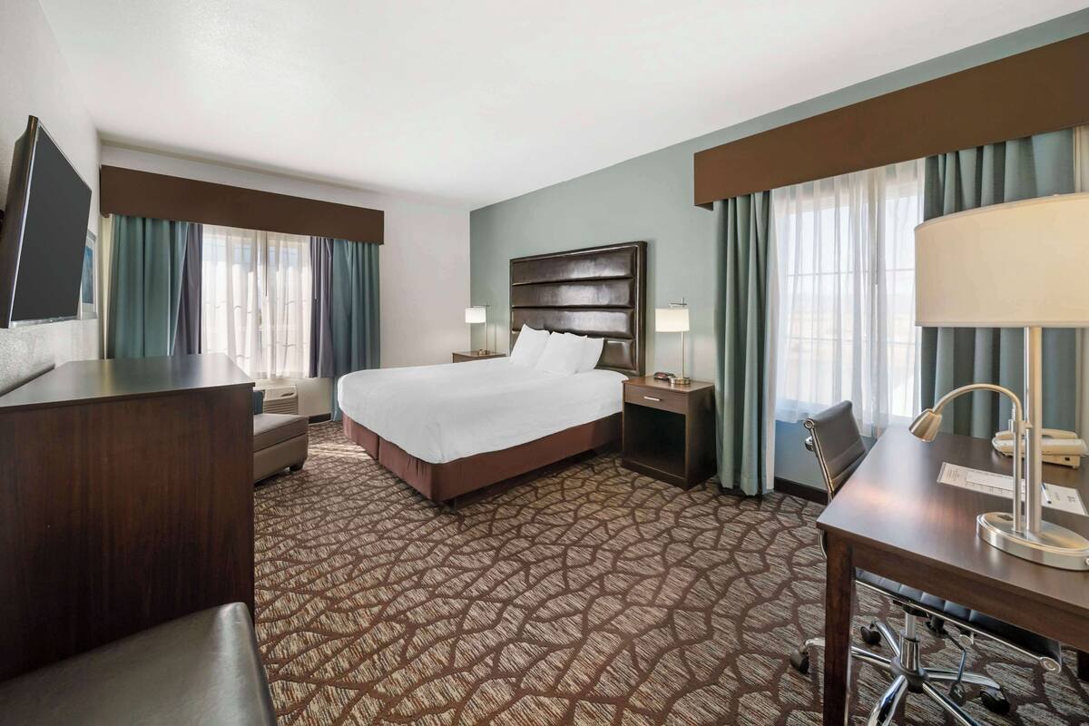 A hotel room with a large bed, a desk, a chair, a TV, and a desk lamp.