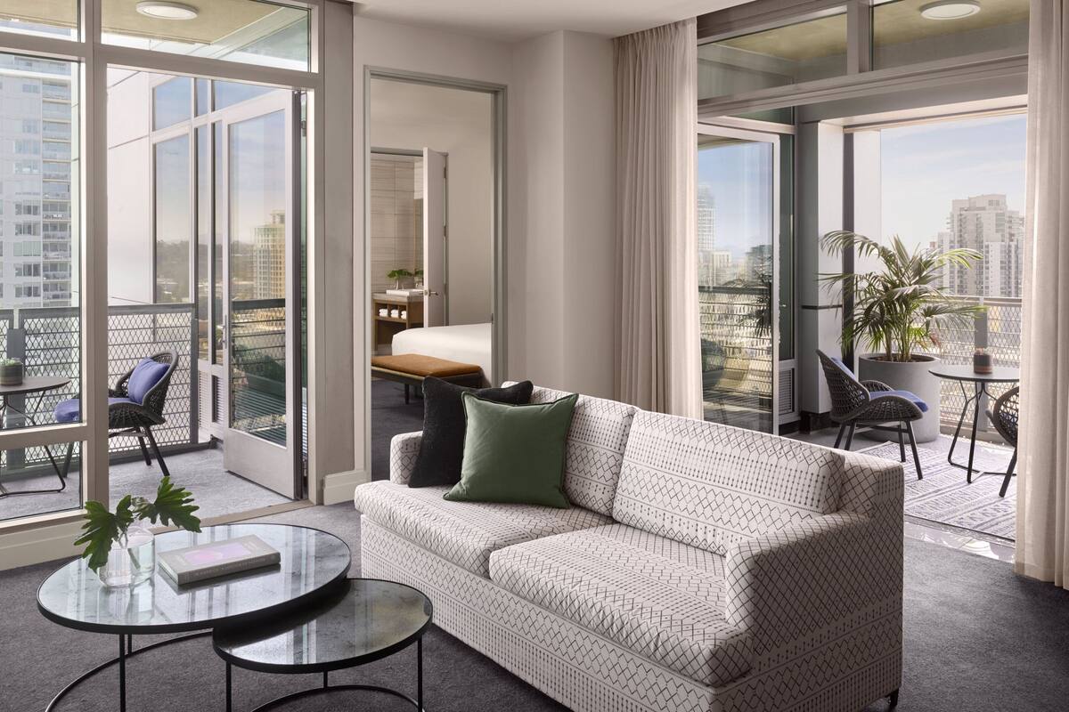 Ein modernes Wohnzimmer mit einer gemusterten Couch, einem Glastisch und Blick auf die Stadt durch große Fenster.