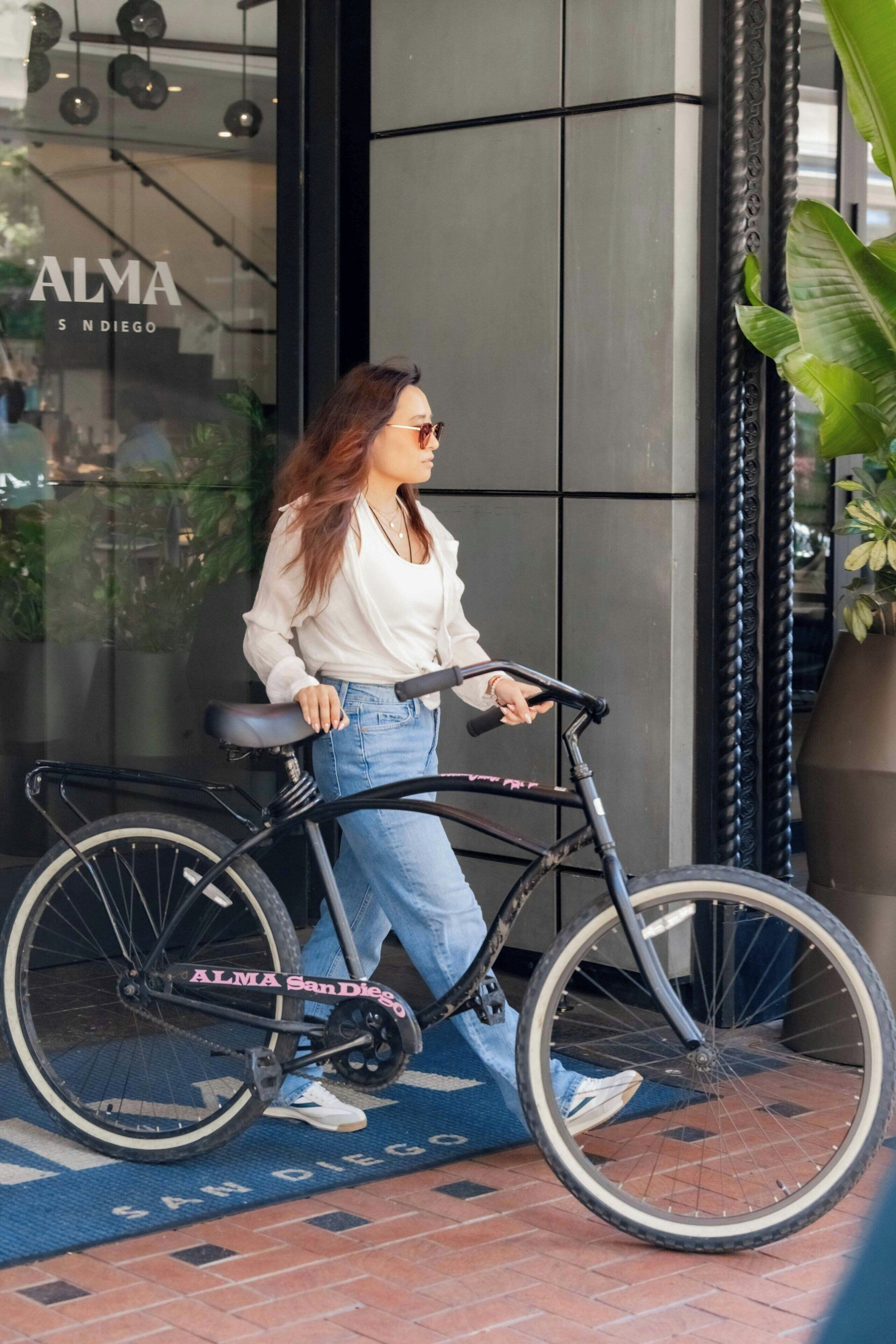 A person with a bicycle in front of a building with a glass door, a blue mat on the ground, and a plant to the right.