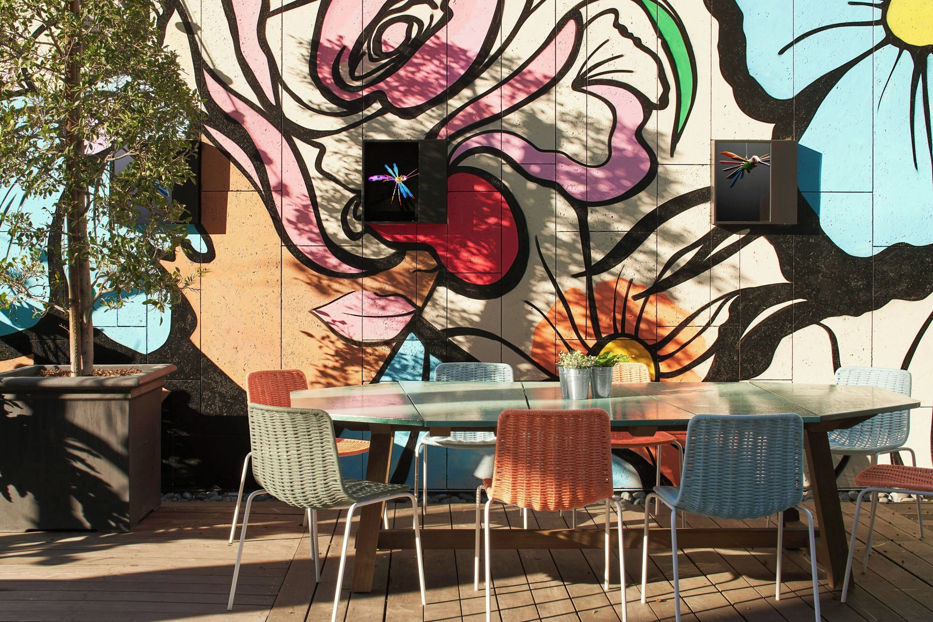 An outdoor dining area with a mural, a table, and chairs.