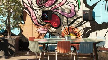 An outdoor dining area with a mural, a table, and chairs.