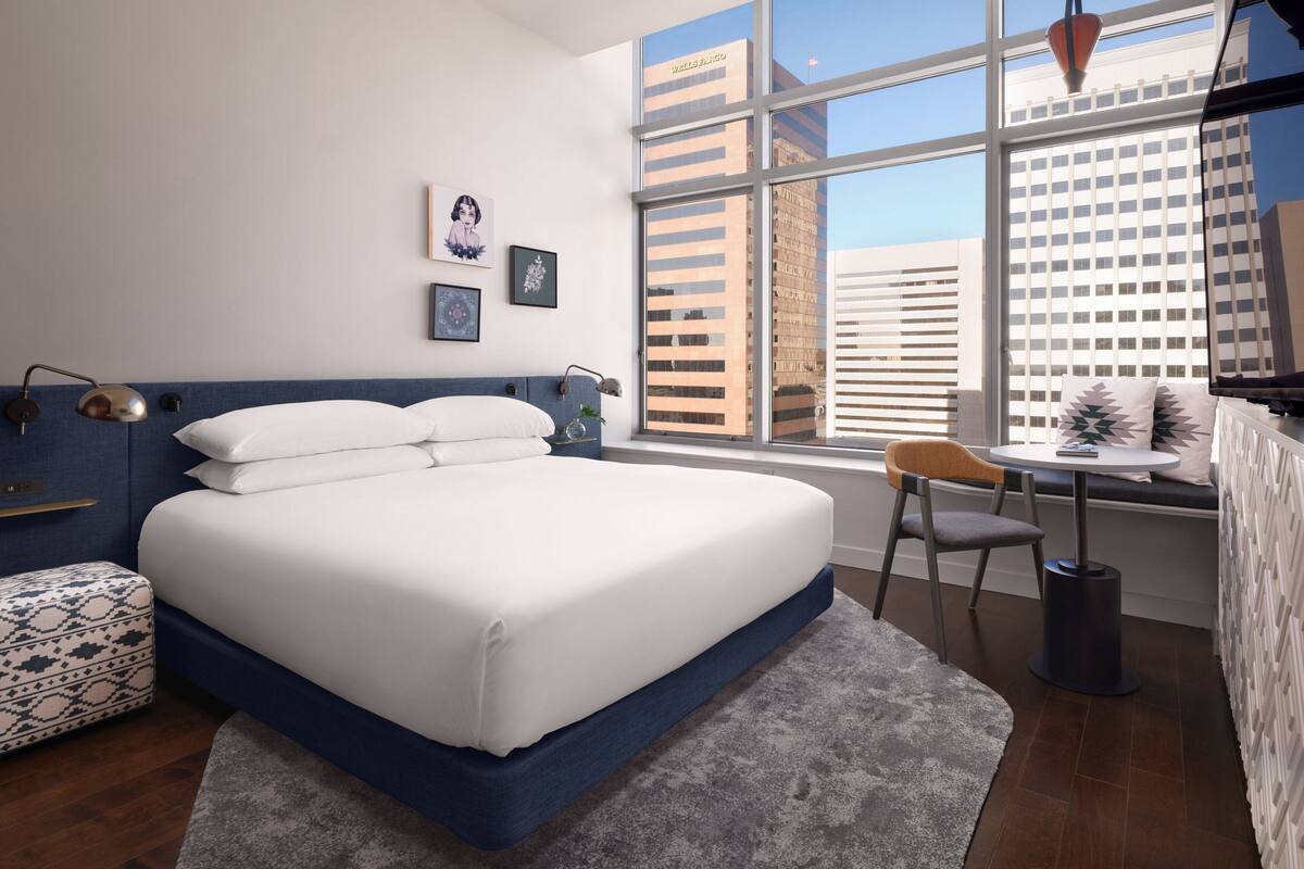 Ein modernes Schlafzimmer mit einem großen Bett, einem kleinen Tisch und einem Fenster mit Blick auf die Stadt.