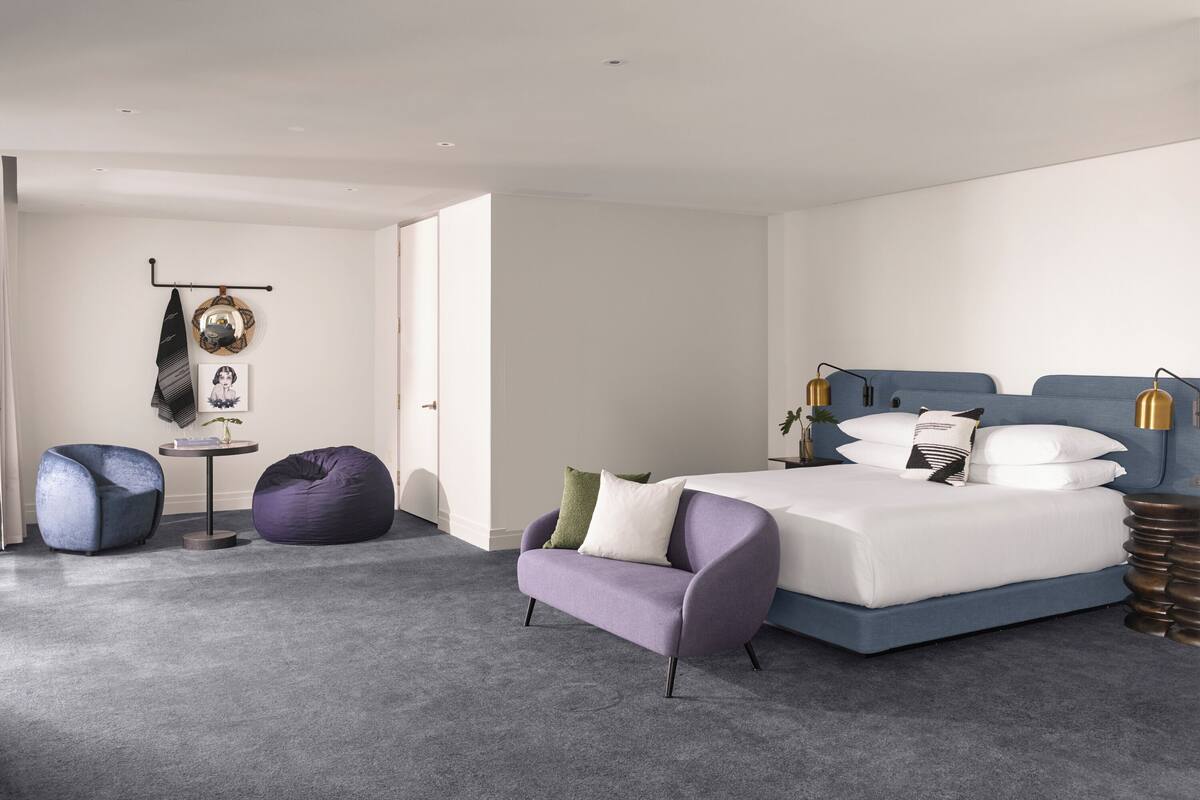 Ein modernes Schlafzimmer mit einem Bett, zwei Sofas, einem runden Tisch und einer Wandlampe.