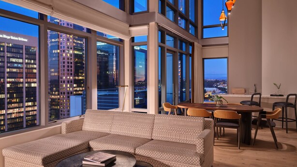 A modern living room with a large sectional sofa, a dining table with chairs, and large windows offering a city view. - Alma San Diego Downtown, a Tribute Portfolio Hotel (San Diego)