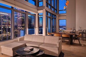 Een moderne woonkamer met een grote hoekbank, een eettafel met stoelen en grote ramen met uitzicht over de stad.