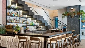 A modern bar area with a long counter, multiple stools, and a staircase leading to an upper level. - Alma San Diego Downtown, a Tribute Portfolio Hotel (San Diego)