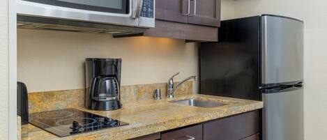 A compact kitchen with a microwave, coffee maker, sink, and a refrigerator.