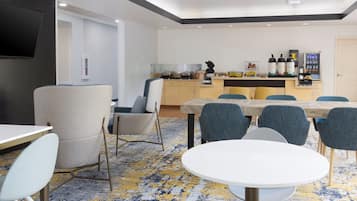 A modern hotel room with a dining area, a kitchen with appliances, and a TV mounted on the wall.
