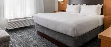 Une chambre d’hôtel avec un grand lit, une table de chevet, une lampe, une fenêtre avec des rideaux et un radiateur.