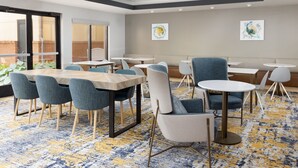 Un espace de détente moderne offrant différents types de sièges, notamment des tables et des chaises, ainsi qu’un tapis à motifs et des œuvres d’art accrochées aux murs.