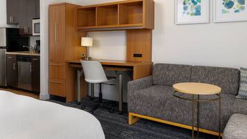 A hotel room with a kitchenette, a desk with a chair, a sofa, and a small round table.
