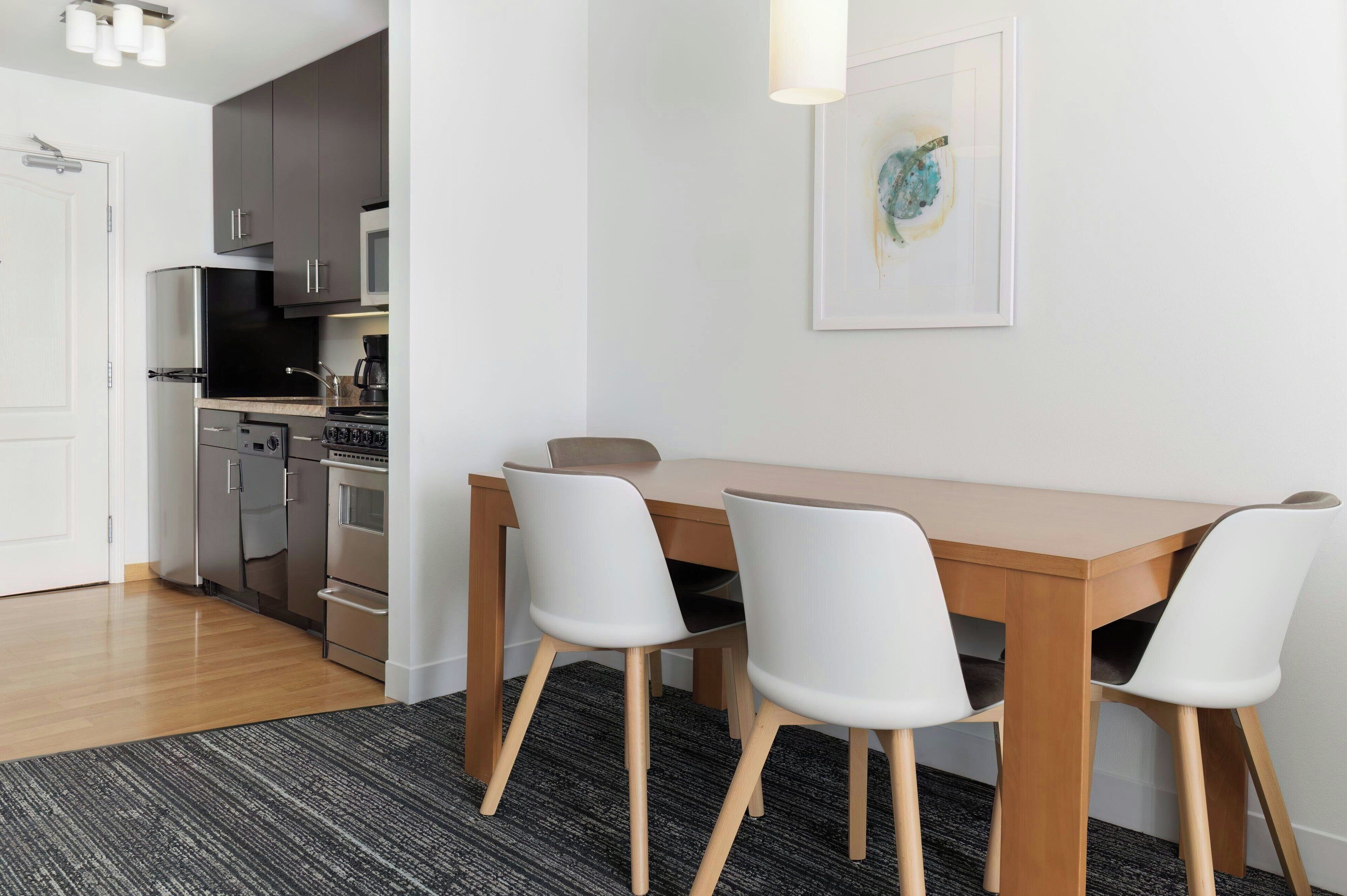 Una cocina compacta con electrodomésticos modernos, una mesa de comedor con cuatro sillas y una obra de arte enmarcada en la pared.